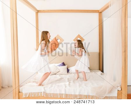 Two little girls fighting with pillows on the bed. Two sisters having pillow fight at bedroom. Sublings playing together