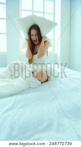 Young caucasian woman covering her head and ears with pillows.