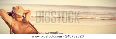 Shirtless man relaxing on deck chair at beach