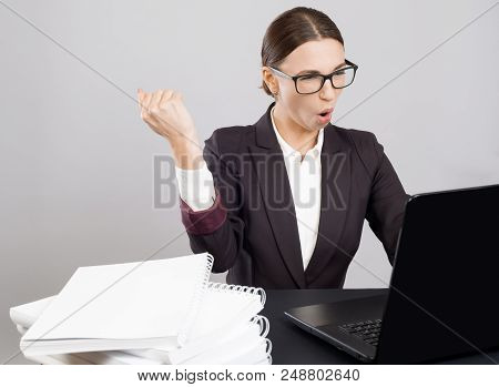 Seccessful Business Woman Sitting At The Desk With Papers And Books With Laptop Holding Her Fist Up