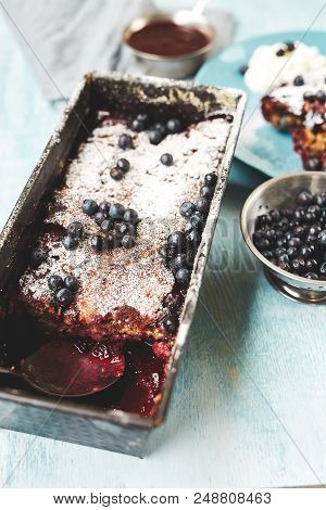 Closeup Berry Crumble In The Baking-tin And Small Bowl With Blueberries On The Blue Wooden Table. To