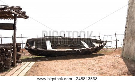 Old Dilapidated Black Wooden Boat With A One-storey House, A Well And A Hill In Russian Cossack Vill