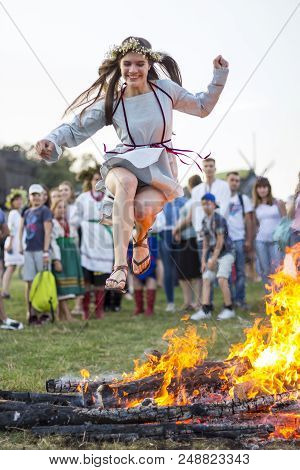 Kyiv, Ukraine - July 6, 2018: Young Girl Jumps Over The Flames Of Bonfire During The Traditional Sla