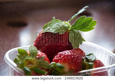 Strawberry In Plastic Box And Grass On Brown Rable