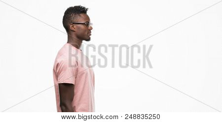 Young african american man wearing pink t-shirt looking to side, relax profile pose with natural face with confident smile.