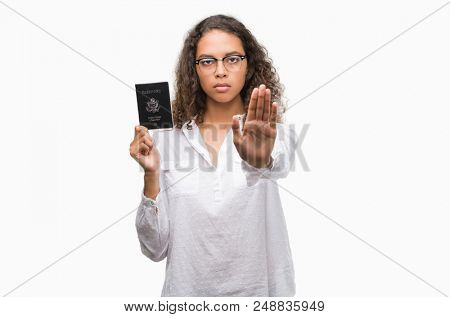 Young hispanic woman holding passport of United States of America with open hand doing stop sign with serious and confident expression, defense gesture