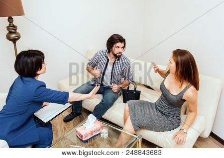 Guy Is Sitting Besides His Wife And Holding Fingers In Fist. He Is Ready To Hit Her. Young Woman Is 