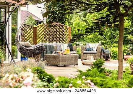 Rattan Garden Furniture And Hanging Chair On Wooden Terrace Of House. Real Photo