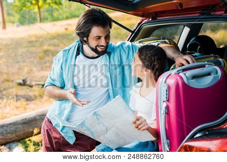Father And Daughter Looking At Each Other And Holding Map At Car Trunk