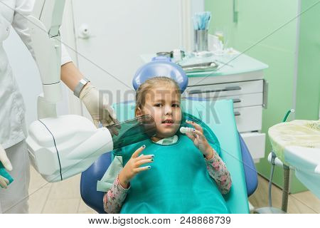 Child With A Mother At A Dentist's Reception. The Girl Lies In The Chair, Behind Her Mother. The Doc