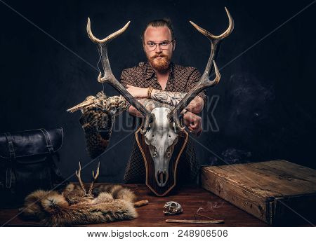 Redhead Taxidermist Hipster Male In Sunglasses Dressed In A Brown Shirt, Standing Near A Table With 