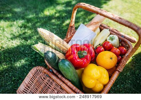Close Up View Of Basket With Baget And Vegetables For Picnic On Green Grass