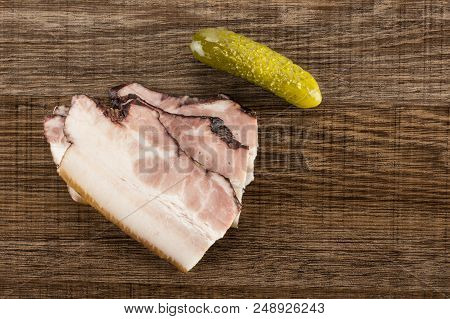 Group Of Three Slices Of English Bacon With A Salted Cucumber Flatlay On Brown Wood