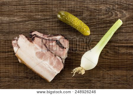 Group Of Three Slices Of English Bacon With One Salted Cucumber And Spring Onion Flatlay On Brown Wo