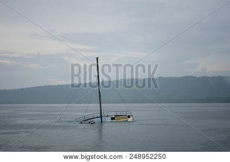 A Half-sunken Yacht Is In A Bay, Its Mast Rising Up Into The Overcast Sky. Some Children Are Swimmin