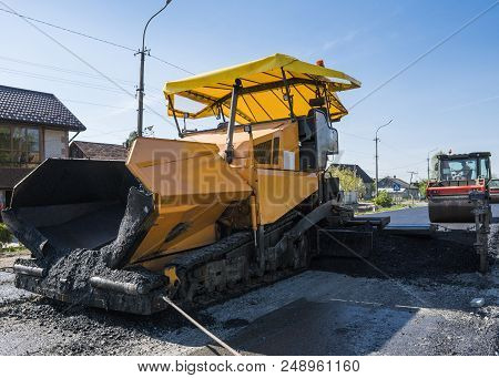 Worker Operating Asphalt Paver Machine During Road Construction And Repairing Works. A Paver Finishe