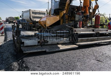 Worker Operating Asphalt Paver Machine During Road Construction And Repairing Works. A Paver Finishe