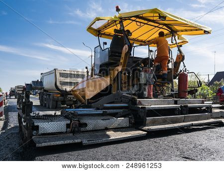 Worker Operating Asphalt Paver Machine During Road Construction And Repairing Works. A Paver Finishe