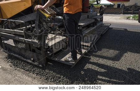 Worker Operating Asphalt Paver Machine During Road Construction And Repairing Works. A Paver Finishe