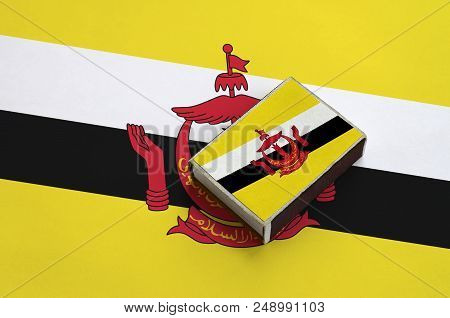 Brunei Darussalam Flag  Is Pictured On A Matchbox That Lies On A Large Flag.
