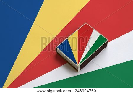 Seychelles Flag  Is Pictured On A Matchbox That Lies On A Large Flag.