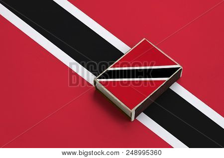 Trinidad And Tobago Flag  Is Pictured On A Matchbox That Lies On A Large Flag.