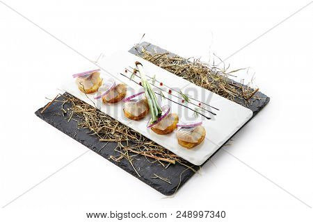 Herring Canape with Potato and Onion on Natural Rustic Background. Beautiful Creative Sea Food Design of Fish Fillet with Scallions on Dry Hay and Black Slate