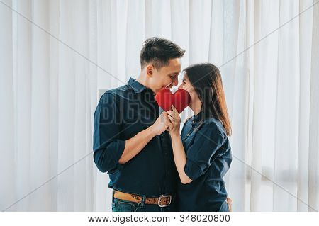 Romantic Happy Asian Couple In Love Kissing Behind Heart Shaped Red Pillow In Room. Vanlentine Day C
