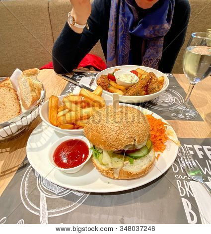 Overhead View Of Woman Eating Delicious Tasty Fish And Chips Next To Copious Portion With Burger And