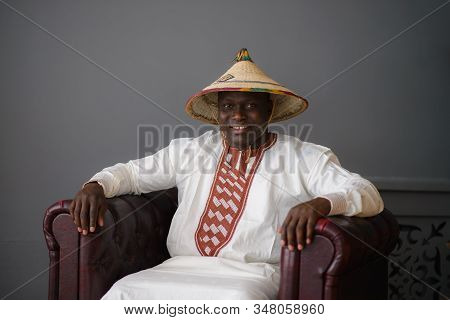 Handsome African Man In Traditional White Dress And Fulani Hat On Gray Background