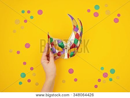 Woman Hand Holding  Festive, Colorful Mardi Gras Or Carnivale Mask Over Yellow Background. Party Inv