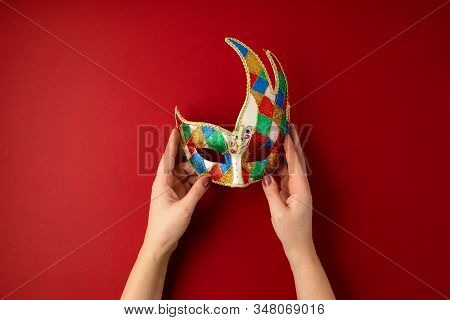 Woman Hand Holding  Festive, Colorful Mardi Gras Or Carnivale Mask Over Red Background. Party Invita