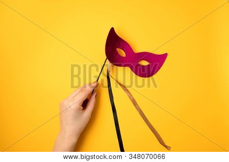Woman Hand Holding  Festive, Colorful Mardi Gras Or Carnivale Mask Over Yellow Background. Party Inv