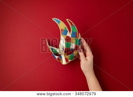Woman Hand Holding  Festive, Colorful Mardi Gras Or Carnivale Mask Over Red Background. Party Invita