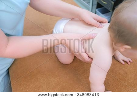 Professional Doctor Masseur Making Massage To Baby On Back In Clinic. Mom Playing Toy With Baby. The