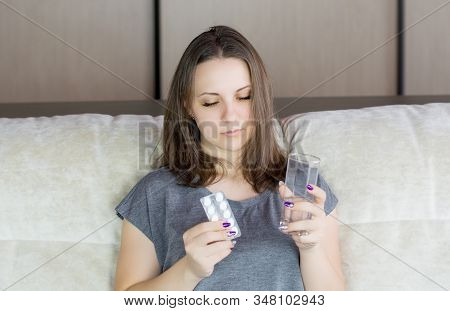 Woman Suffers Headache, Takes Pill While Sitting In Sofa With Glass Of Water.