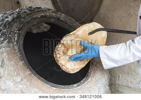 A Male Cook Takes A Fresh Tortilla From The Oven. The Process Of Baking Bread In A Traditional Georg