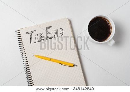 The End Text On Copybook. Notepad, Pen And Cup Of Coffee On White Background. Top View.