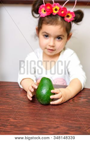 Little Cute Smiling Black Hair Girl Holding Green Avocado. Healthy Food For Children Concept. Select