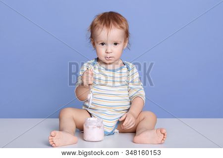 Image Of Adorable Little Child Wearing Stripped Bodysuit, Sitting Isolated Over Blue Studio Backgrou