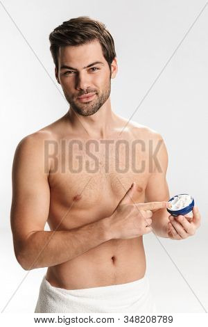 Photo of handsome half-naked man in bath towel applying facial cream isolated over white background
