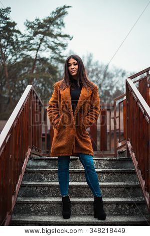Portrait Of Beautiful Brunette Girl (woman) In Orange Fashion Coat In Highheels - Photo On Stairs Wi
