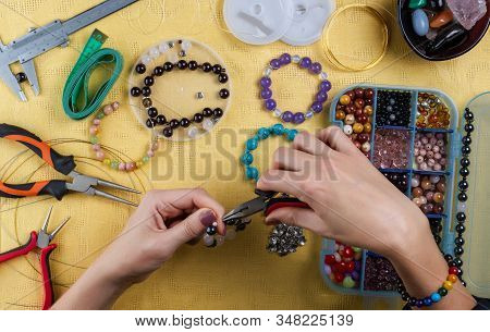 Jewelry Making. Making A Bracelet Of Colorful Beads. Female Hands With A Tool On A Yellow Background