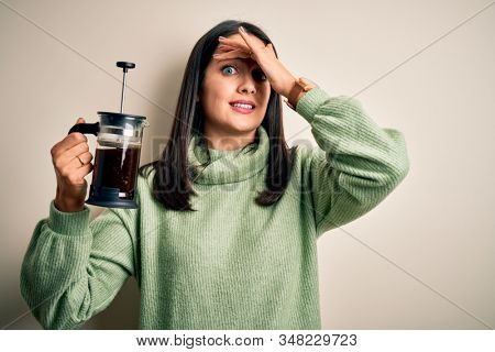 Young woman with blue eyes making cafe using coffee maker standing over white background stressed with hand on head, shocked with shame and surprise face, angry and frustrated. Fear and upset