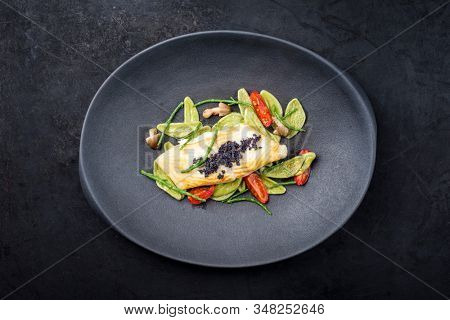 Gourmet fried Italian sea bass fish filet with spinach pasta, caviar and tomatoes as top view on a modern design plate with copy space 