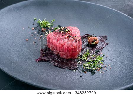 Gourmet fish tartar raw from tuna fillet with seaweed, umeboshi and Japanese spice as closeup on modern design plate 