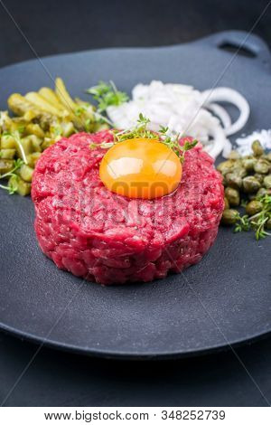 Gourmet tartar raw from beef fillet with yellow of the egg and gherkin with capers and onion rings as closeup on modern design plate 