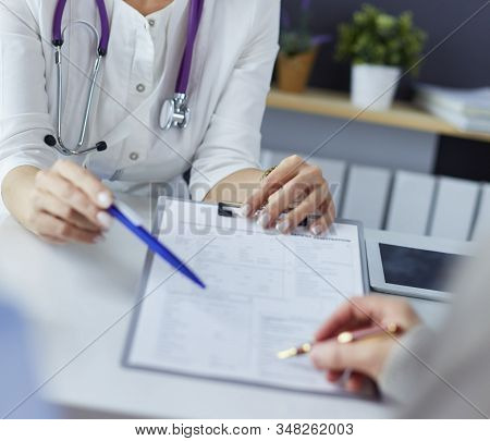 Doctor And Patient Examining A File With Medical Records, She Is Sitting On A Wheelchair
