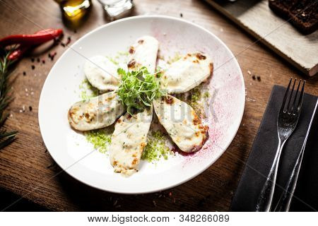 Cooked green mussels with parmegano and cream cheese served on white plate in restaurant