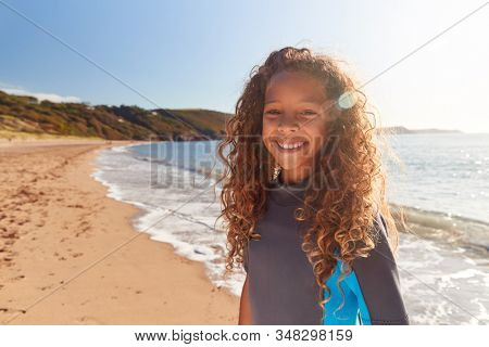 Portrait Of Young Girl Wearing Wetsuit Standing By Waves On Summer Beach Vacation